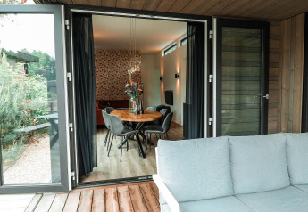 Blick von einer Holzterrasse in eine moderne Lodge mit Essbereich, Sesseln und stilvoller Inneneinrichtung.