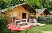 Tienda safari Villatent Wood en Camping Domaine du Logis en Francia con hamaca y zona de estar exterior.