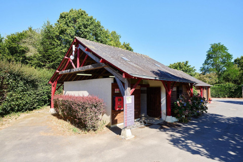 Edificio de recepción con vigas rojas en Camping Domaine du Logis en Francia, rodeado de naturaleza.