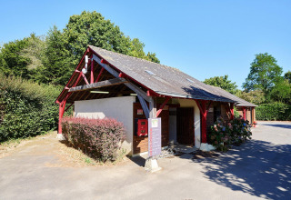 Edificio de recepción con vigas rojas en Camping Domaine du Logis en Francia, rodeado de naturaleza.