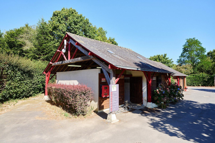 Bâtiment d’accueil avec poutres rouges au Camping Domaine du Logis en France, entouré de verdure.