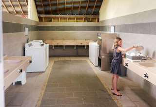 Una niña lava platos en la cocina común de Camping Domaine du Logis, Villatent Wood, Francia.