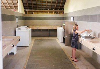 Una ragazza lava i piatti nell'area cucina comune al Camping Domaine du Logis, Villatent Wood, Francia.