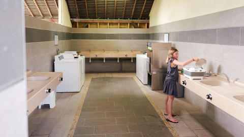 Una ragazza lava i piatti nell'area cucina comune al Camping Domaine du Logis, Villatent Wood, Francia.