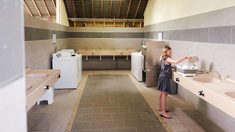 Een meisje wast af in de gezamenlijke keuken van Camping Domaine du Logis, Villatent Wood, Frankrijk.