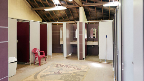 Área de baños limpia y amplia con cabinas y lavabos en Camping Domaine du Logis, Francia.