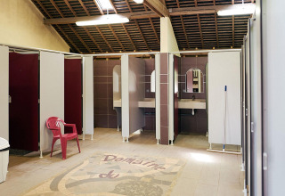 Área de baños limpia y amplia con cabinas y lavabos en Camping Domaine du Logis, Francia.