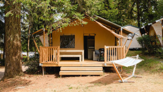 Wooden lodge with porch and hammock at Villatent Outback, Camping Le Sequoia in France, surrounded by trees.
