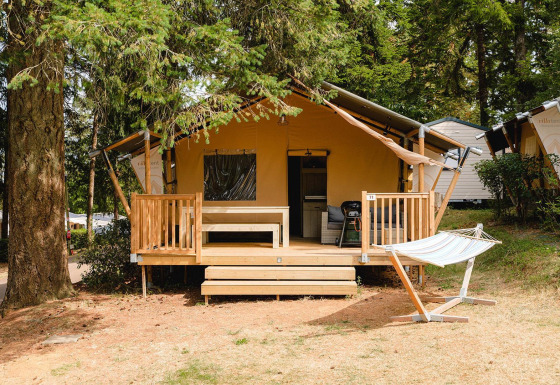 Houten lodge met veranda en hangmat bij Villatent Outback op Camping Le Sequoia in Frankrijk, omgeven door bos.