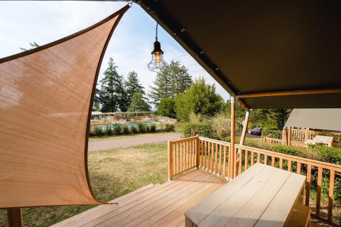 View from Villatent Outback lodge at Camping Le Sequoia in France, featuring wooden terrace and pool area.