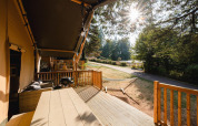 Sonnige Terrasse mit Holzmöbeln, Grill und Hängematte in der Villatent Outback am Camping Le Sequoia, Frankreich.