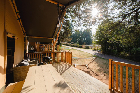 Terraza soleada con muebles de exterior, barbacoa y hamaca en Villatent Outback, Camping Le Sequoia, Francia.