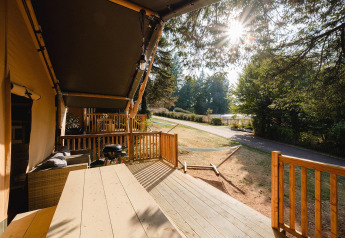 Sonnige Terrasse mit Holzmöbeln, Grill und Hängematte in der Villatent Outback am Camping Le Sequoia, Frankreich.
