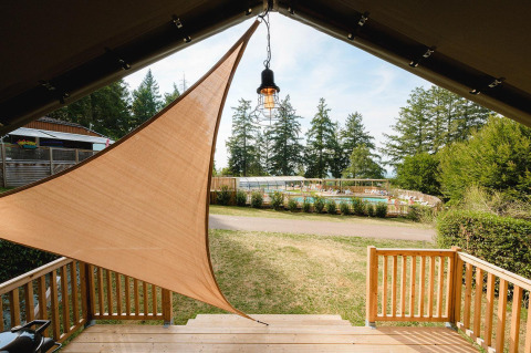 Vista da una lodge con tenda parasole sulla piscina e alberi verdi al Camping Le Sequoia, Francia.