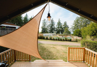 Zicht vanuit een lodge met zonnedoek op zwembad en groene bomen bij Camping Le Sequoia, Frankrijk.