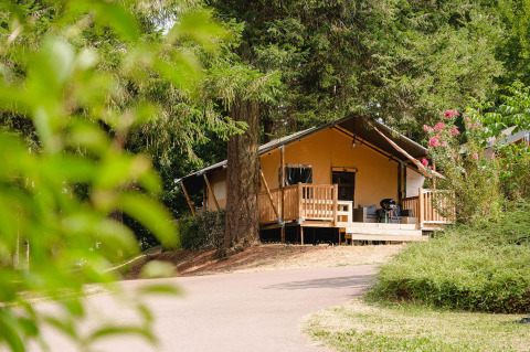 Villatent Outback lodge bij Camping Le Sequoia in Frankrijk, omgeven door bomen en groene natuur.