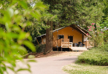 Villatent Outback lodge ved Camping Le Sequoia i Frankrig, omgivet af grønne træer og natur.