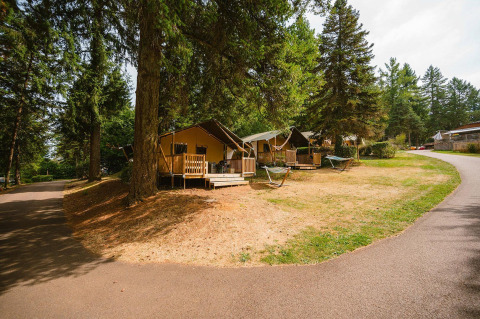 Villatent Outback lodges bij Camping Le Sequoia in Frankrijk, omgeven door bomen, hangmatten en een pad.