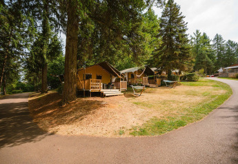 Villatent Outback lodges bij Camping Le Sequoia in Frankrijk, omgeven door bomen, hangmatten en een pad.