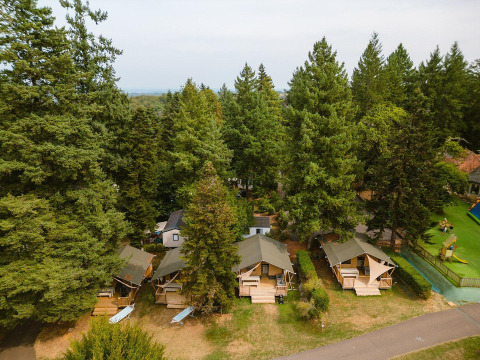 Vista aérea de Villatent Outback en Camping Le Sequoia, Francia, con cabañas entre altos árboles verdes.