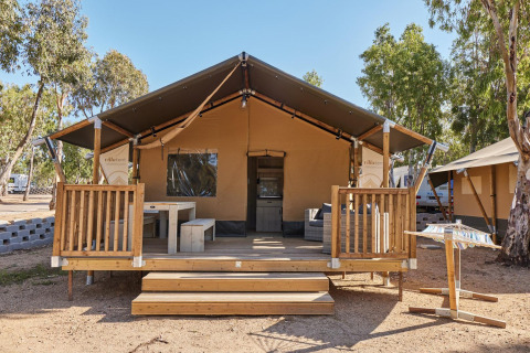 Villatent Outback lodge met houten terras bij Camping Village Baia Blu La Tortuga, Italië, omgeven door bomen.