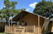 Lodge Villatent Outback con terraza de madera, rodeado de árboles verdes bajo un cielo azul claro y soleado.