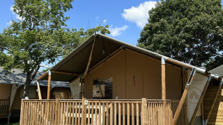 Villatent Outback lodge med træveranda under en klar blå himmel og grønne træer omkring telthytten.