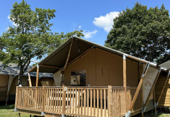 Villatent Outback lodge met een houten terras, omgeven door bomen onder een stralend blauwe hemel.