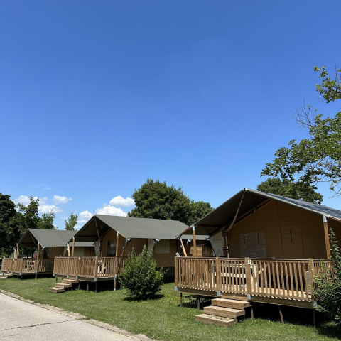 Vier lodgetenten bij Villatent Outback met houten veranda’s en gras onder een strakblauwe lucht.