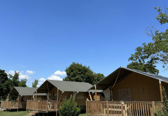 Vier lodgetenten met houten terras bij Villatent Outback, omgeven door groen en blauwe lucht.