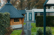 Veluwe Villa lodge bij Vakantiepark De Boshoek in Nederland, met groenstroken en houten huisje.