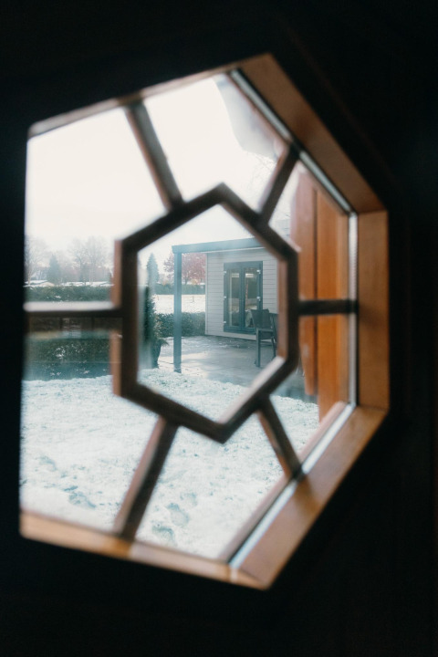 Zicht door een achthoekig raam bij Veluwe Villa in Holiday park De Boshoek, Nederland, met sneeuw buiten.