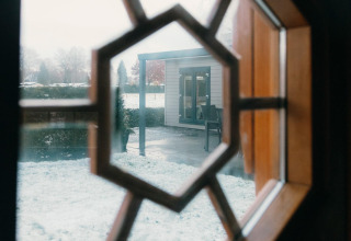 Vista a través de una ventana octogonal en Veluwe Villa, Holiday park De Boshoek, Países Bajos, con nieve afuera.