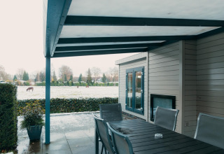Terraza cubierta con mesa y sillas, vista invernal a campo con caballos en Veluwe Villa, De Boshoek, Países Bajos.