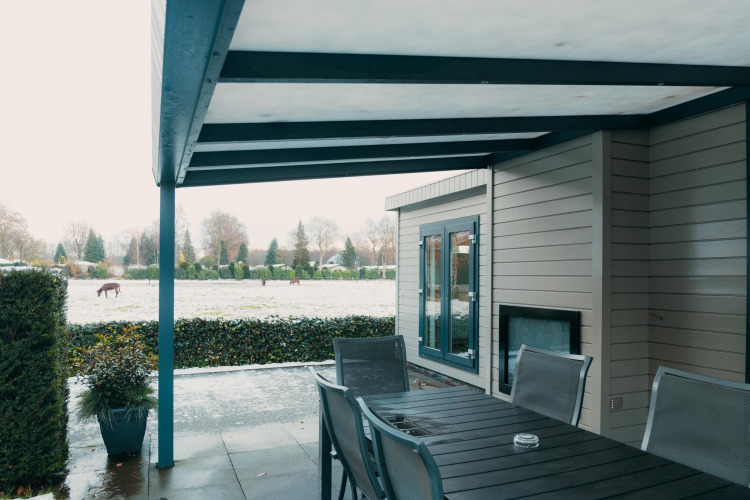 Covered patio with table and chairs, winter view over field with horses at Veluwe Villa, De Boshoek, Netherlands.
