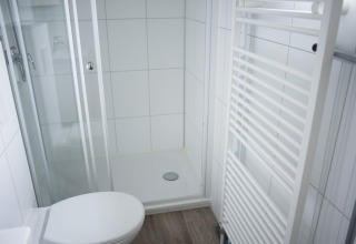 Baño moderno con ducha, inodoro y radiador toallero en Veluwe Villa, Holiday Park De Boshoek, Países Bajos.