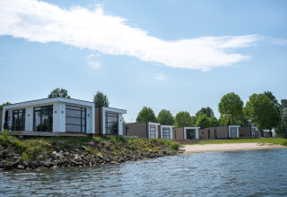 Moderne villaer på Villa Maritiem med store vinduer, tæt på en sø med strand og træer omkring.
