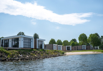 Moderne villa’s bij Villa Maritiem met grote ramen, aan het water en omgeven door bomen.