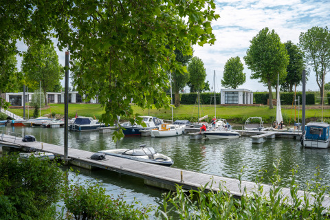Både ligger fortøjet ved en marina foran Villa Maritiem på MarinaPark Bad Nederrijn med grønne træer.