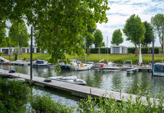 Både ligger fortøjet ved en marina foran Villa Maritiem på MarinaPark Bad Nederrijn med grønne træer.