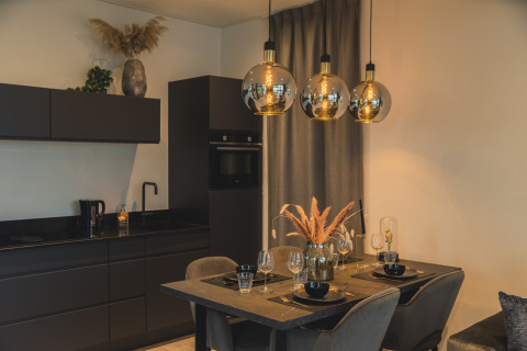 Zona moderna de cocina y comedor en Villa Maritiem de MarinaPark Bad Nederrijn con muebles negros elegantes y lámparas colgantes.