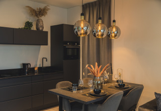 Zona moderna de cocina y comedor en Villa Maritiem de MarinaPark Bad Nederrijn con muebles negros elegantes y lámparas colgantes.