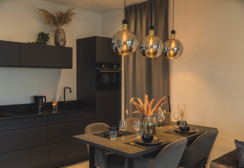 Moderna zona pranzo e cucina a Villa Maritiem nel MarinaPark Bad Nederrijn con arredi neri eleganti e lampade a sospensione.