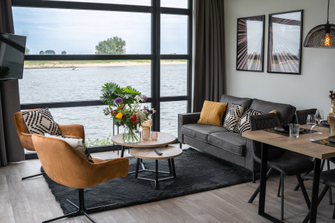 Salón moderno en Villa Maritiem con grandes ventanales, vista al río y elegante decoración interior.