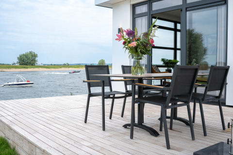 Terraza en Villa Maritiem, MarinaPark Bad Nederrijn, Países Bajos, con mesa, sillas y vista al río.