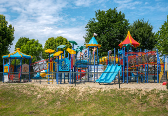Kleurrijke speeltuin aan Villa Maritiem met glijbanen, klimnetten en spelende kinderen onder de bomen.