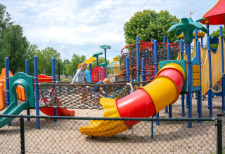 Children playing on a colorful outdoor playground at Villa Maritiem, with trees and fencing around.