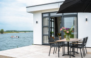 Moderna cabaña frente al lago con terraza, mesa y flores; vista de bote en Villa Maritiem, MarinaPark Bad Nederrijn, Países Bajos.