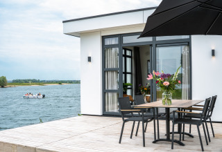 Moderna cabaña frente al lago con terraza, mesa y flores; vista de bote en Villa Maritiem, MarinaPark Bad Nederrijn, Países Bajos.