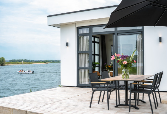 Moderne lodge aan het water met terras, bloementafel en uitzicht op boot bij Villa Maritiem, MarinaPark Bad Nederrijn.